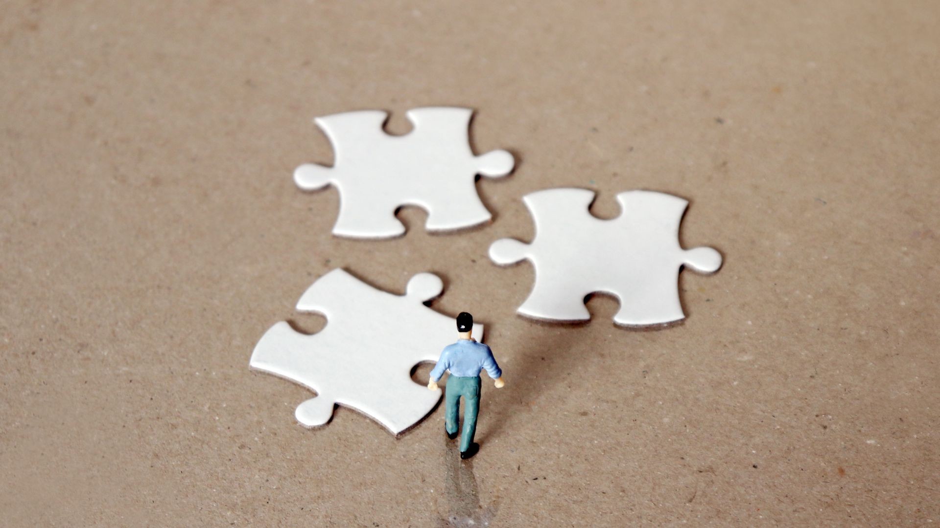 A miniature man staring down three pieces of the puzzle. A miniature man staring down three pieces of the puzzle.